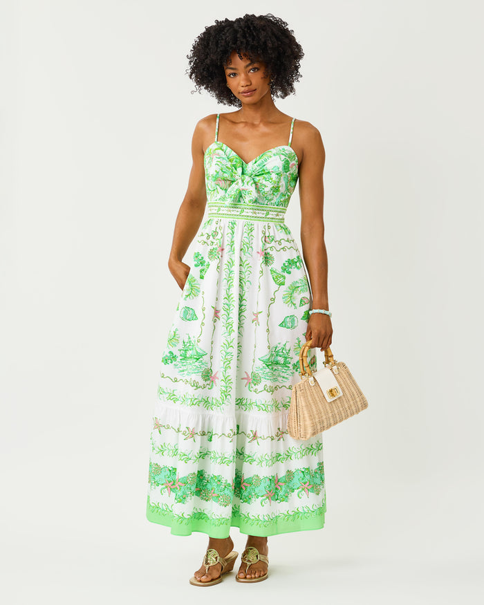 Woman wearing a green and white floral dress with front tie holding a beige handbag on a white background