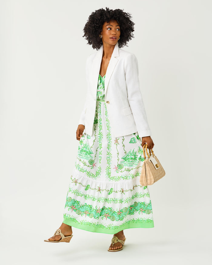 Woman wearing a green and white floral dress with front tie with a white blazer on top on a white background