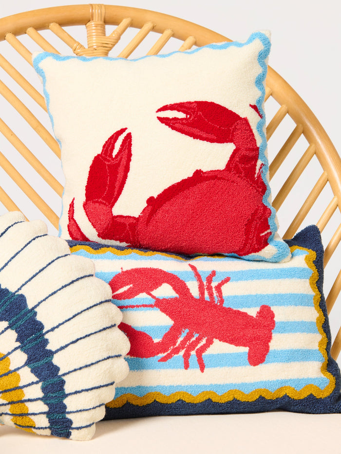 Decorative navy pillow with a red lobster on a blue and white striped background with golden yellow trim on a wicker chair