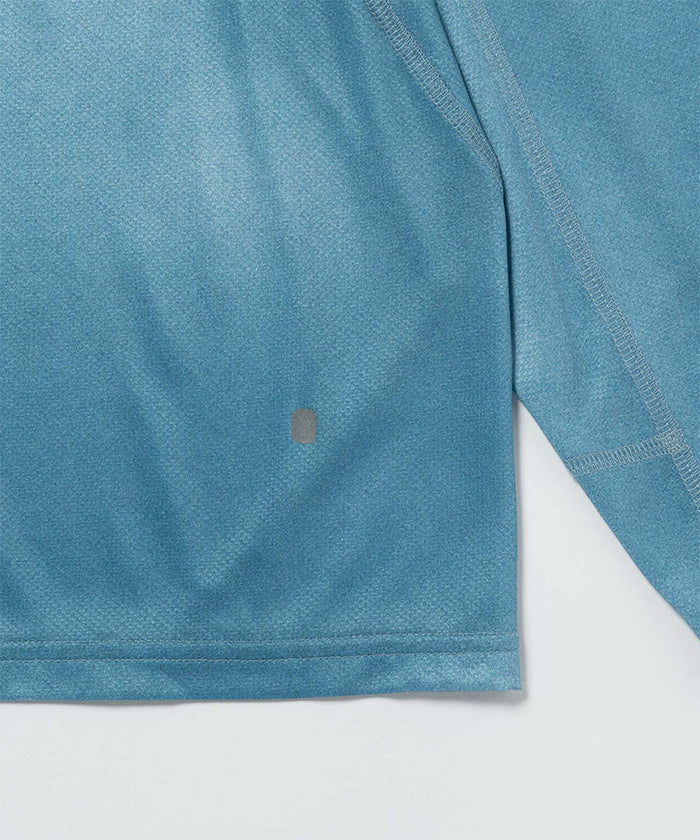 Gramicci blue tie-dye L/S 1st Layer shirt hem detail against a light-tone background.