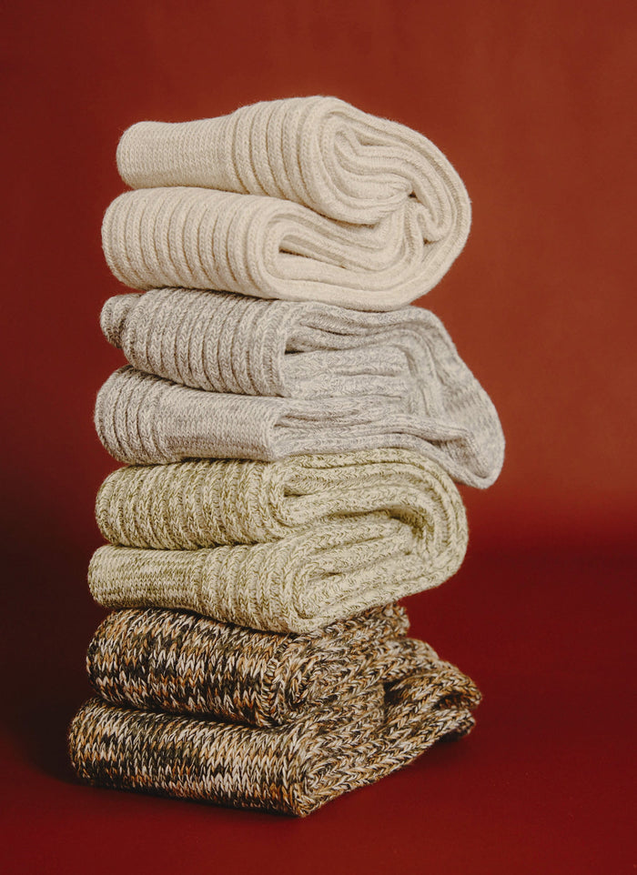 A stack of four pairs of ribbed, marl cotton socks from Percival in neutral colours, set against a rich red background.