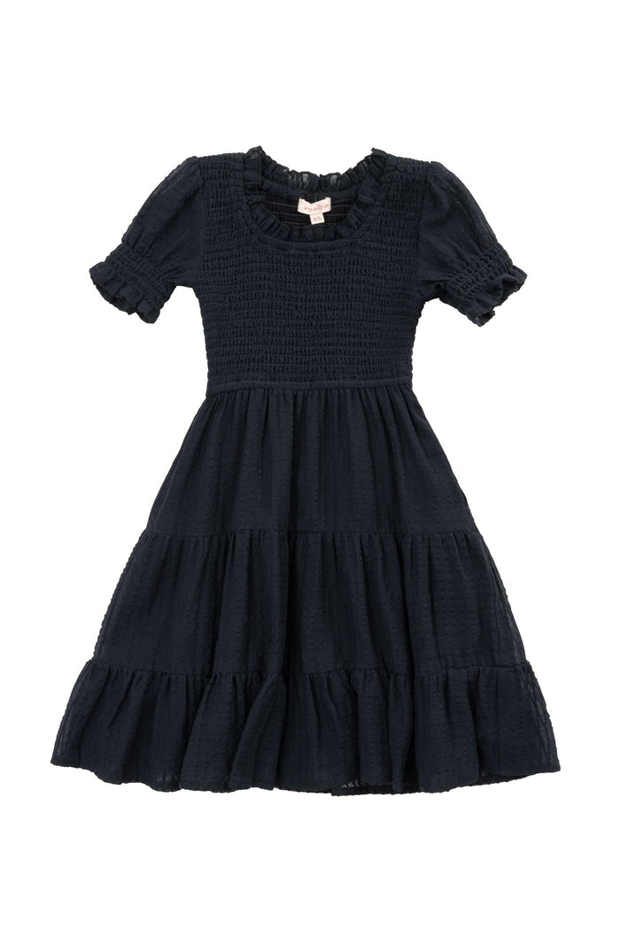 Introducing the Mini Ellery Dress in Black from Ivy City Co—a charming kids’ dress with a smocked bodice, short sleeves adorned with playful ruffle details, and a tiered knee-length skirt. Featuring a ruffled neckline and perfect for coordinating with mom outfits, this dress is beautifully presented against a white background.