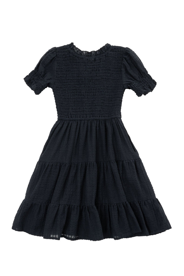 The Mini Ellery Dress in Black by Ivy City Co features a smocked bodice, ruffled short sleeves, and a tiered, flared knee-length skirt. Shown laid flat on a white background, it’s perfect for matching mom in coordinated outfits.
