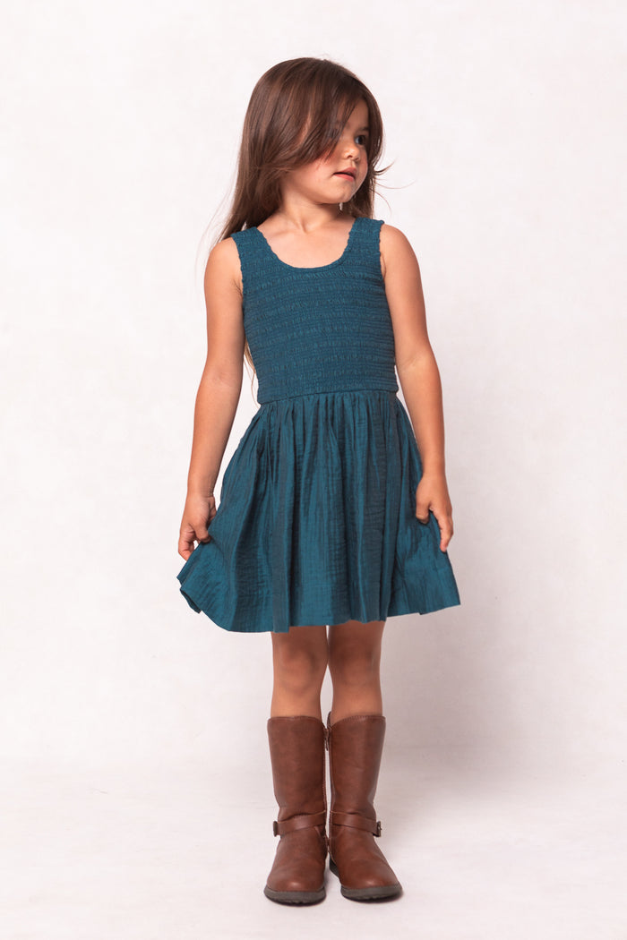Young girl wearing a teal dress and brown boots on a white background