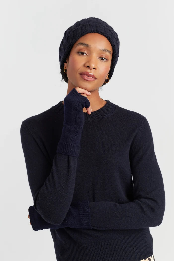 Person wearing a navy sweater, beanie, and gloves on a light gray background