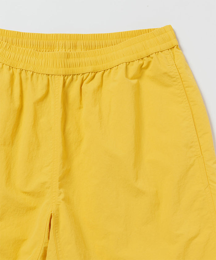 Close-up of banana colored Gramicci Nylon Reef Shorts on a light-tone background.