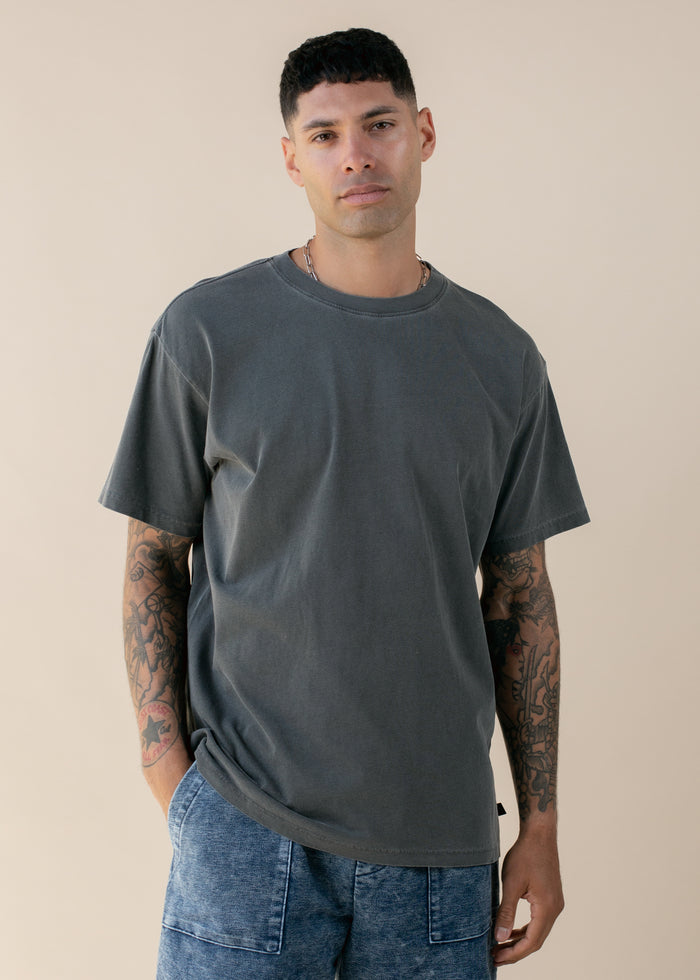 Man wearing a dark gray t-shirt and blue jeans against a beige background