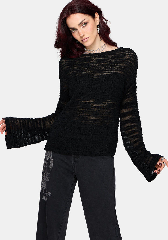 Woman wearing a black distressed jumper with long sleeves and back denim jeans on a white background