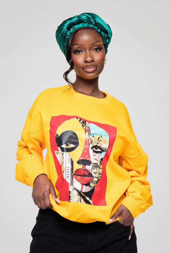 Woman wearing a yellow sweatshirt with a colorful graphic design on a plain background