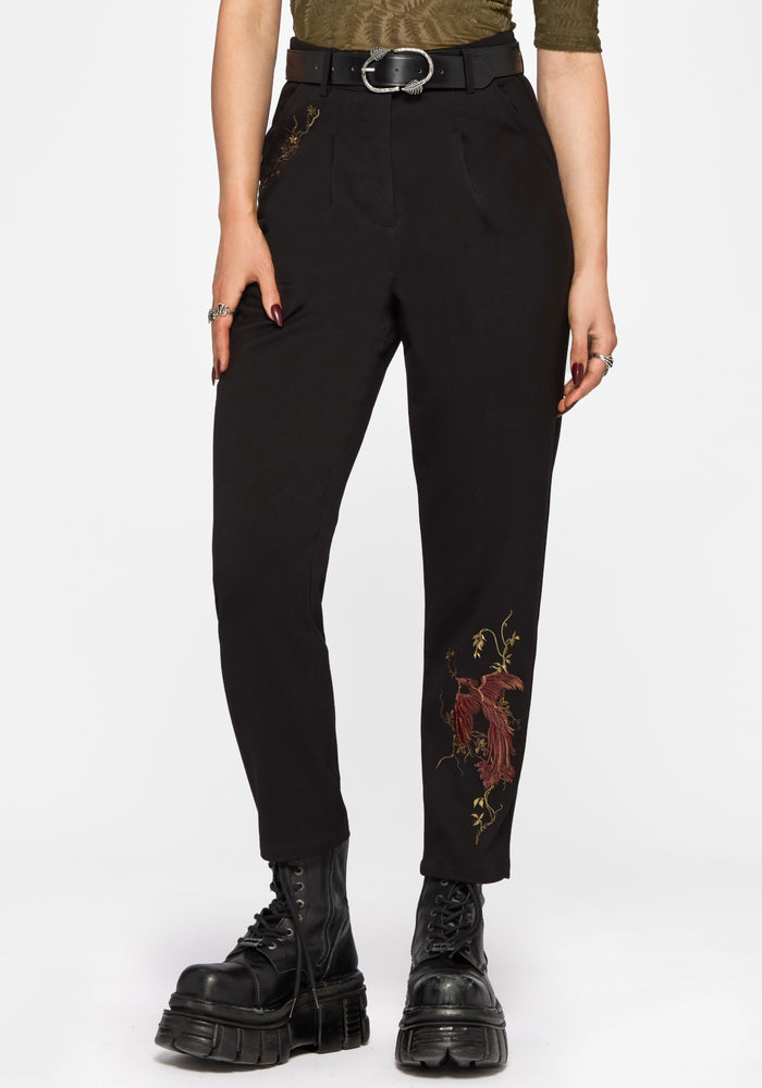 Woman wearing black pants with floral embroidery and black platform boots on a white background