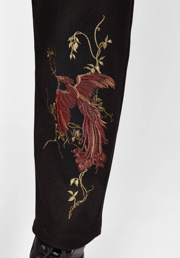 Black pants with red floral embroidery on a white background