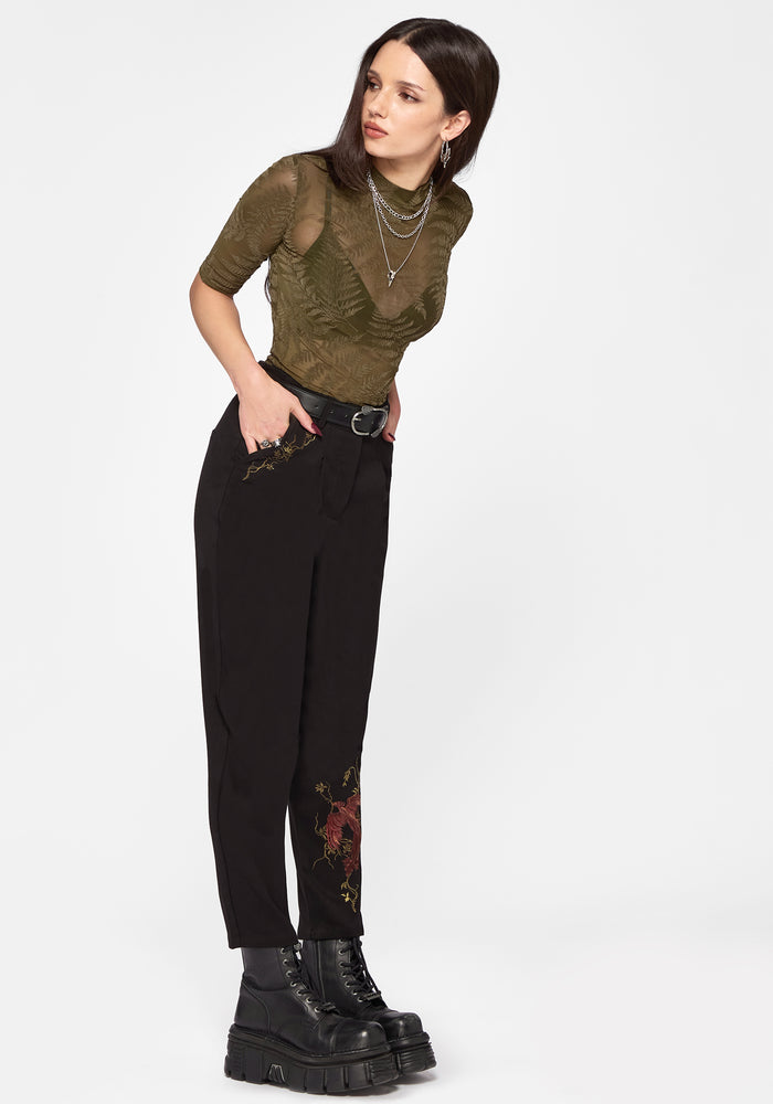 Woman wearing a green top and black pants with floral designs on a white background