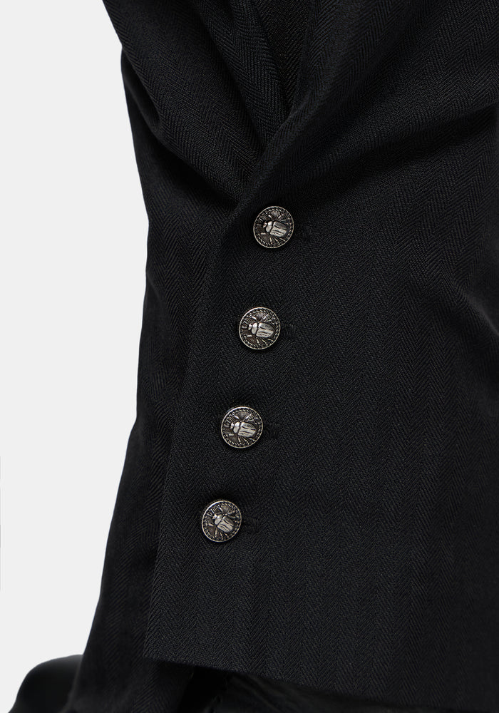 Close-up of black balloon trousers   with four decorative metallic buttons on a light gray background.