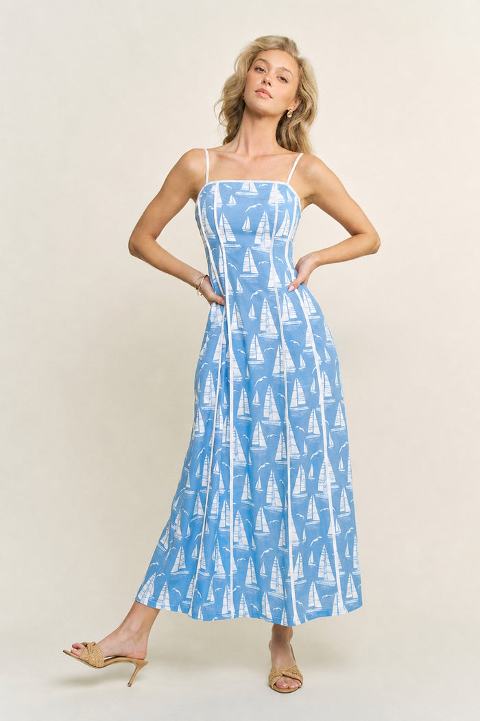 Woman wearing a blue dress with sailboat pattern on a white background with white trim and detailing