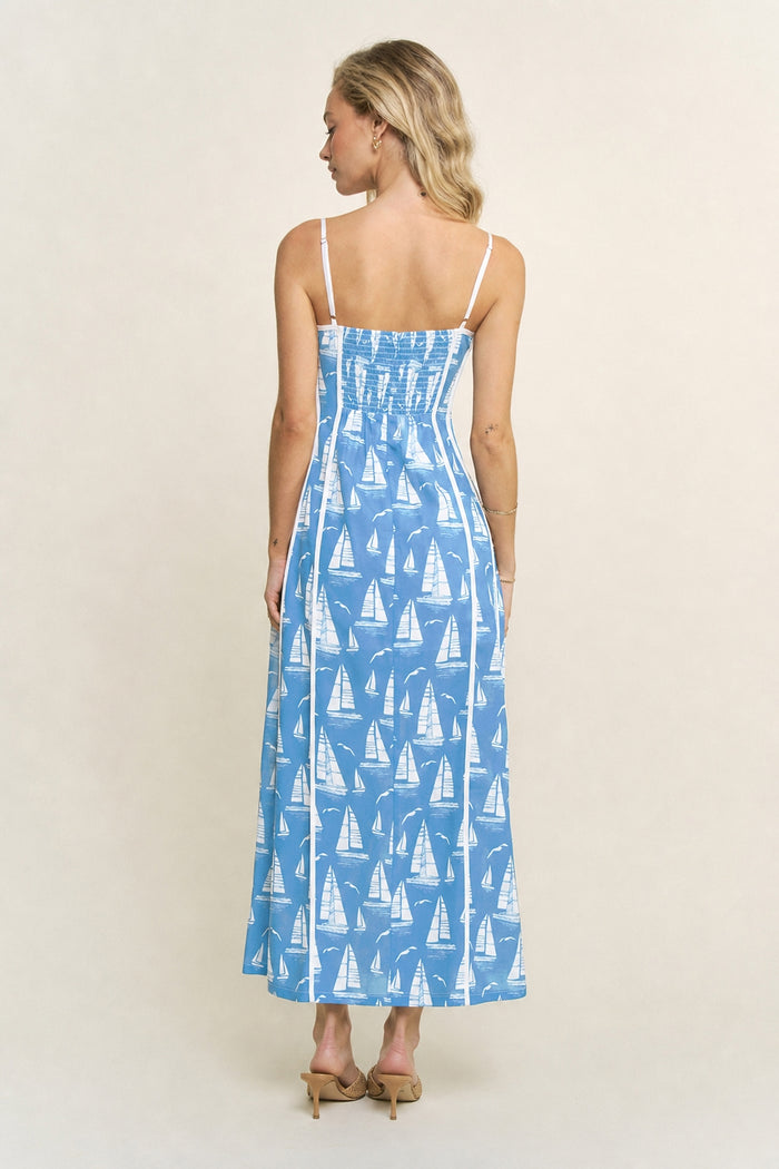 Woman wearing a blue dress with sailboat pattern on a white background with white trim and detailing and adjustable straps