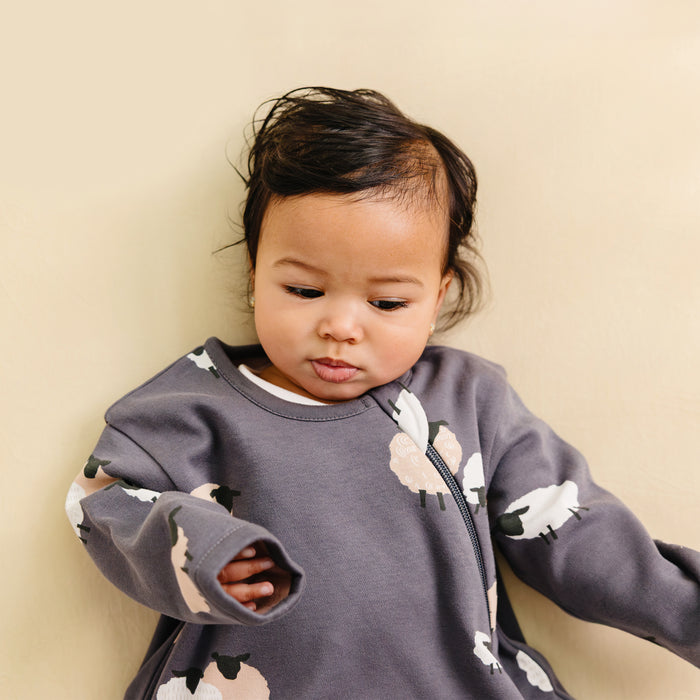 Baby wearing a gray sleep sack with sheep prints against a beige background
