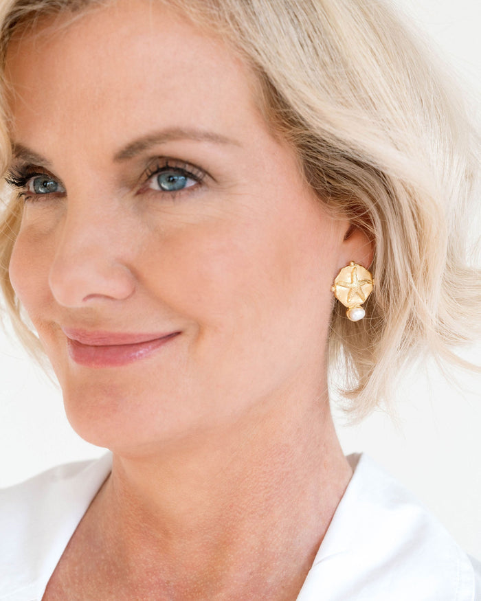 Close-up of a woman wearing gold earrings with a pearl detail on a white background