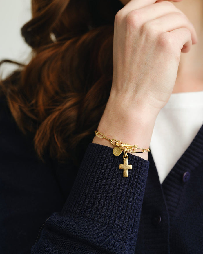 Gold bracelet with charms on a wrist against a dark sweater background