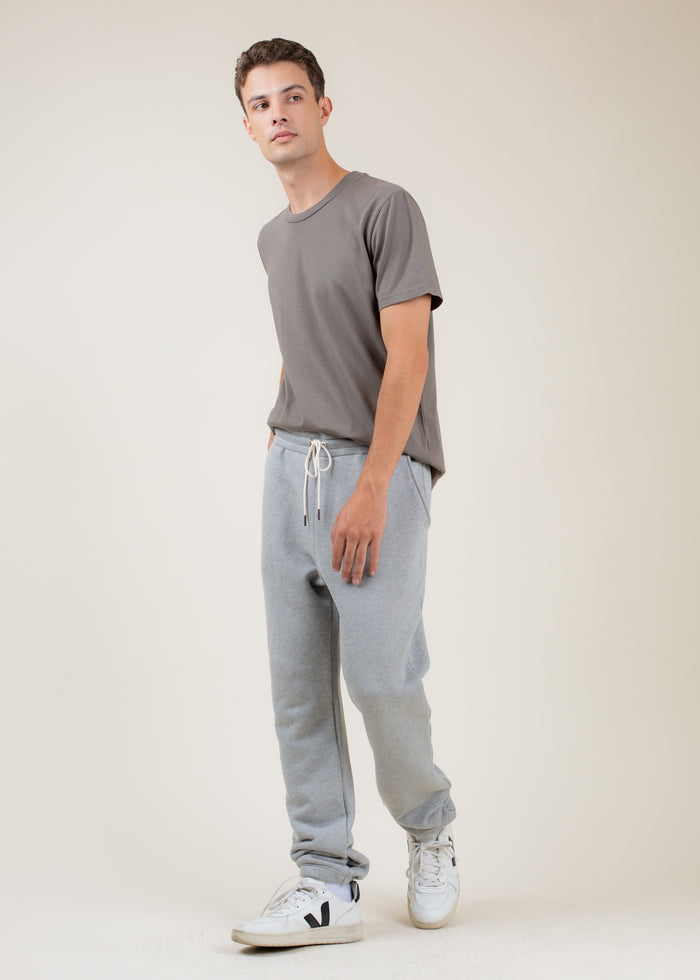 Man wearing a gray t-shirt and light gray sweatpants with white sneakers on a plain background