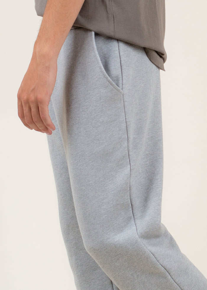 Close up of gray sweatpants worn by a person on a light beige background