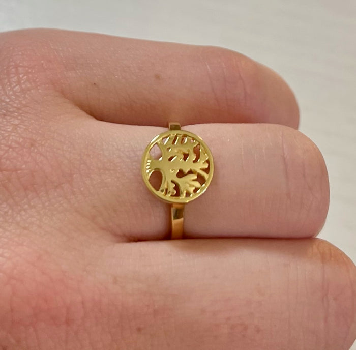 A gold-colored ring with a Tree of Life design on the top, displayed on a person's finger.