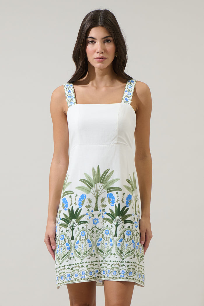 Woman wearing a white dress with blue and green floral patterns on a plain background