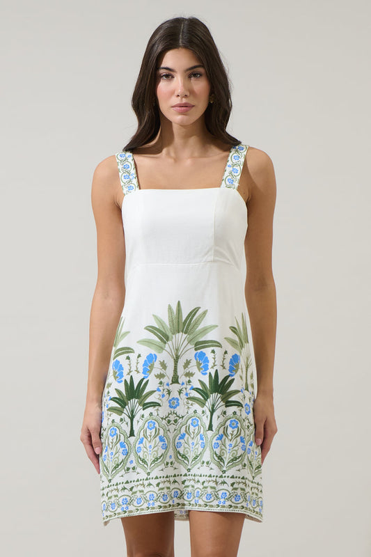 Woman wearing a white dress with blue and green floral patterns on a plain background