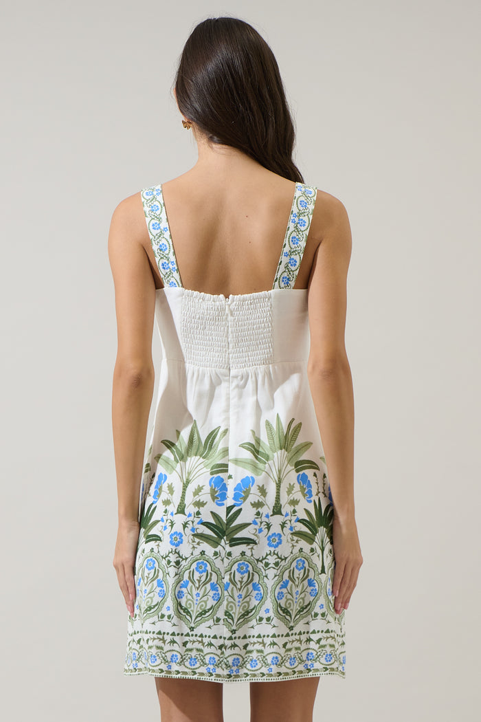 Woman wearing a white dress with blue and green floral patterns on a plain background