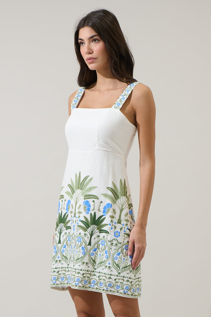 Woman wearing a white dress with blue and green floral patterns on a plain background