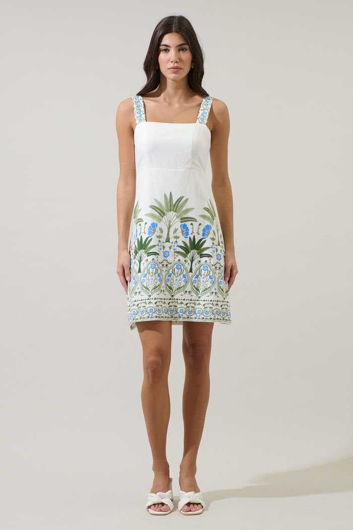 Woman wearing a white dress with blue and green floral patterns on a plain background