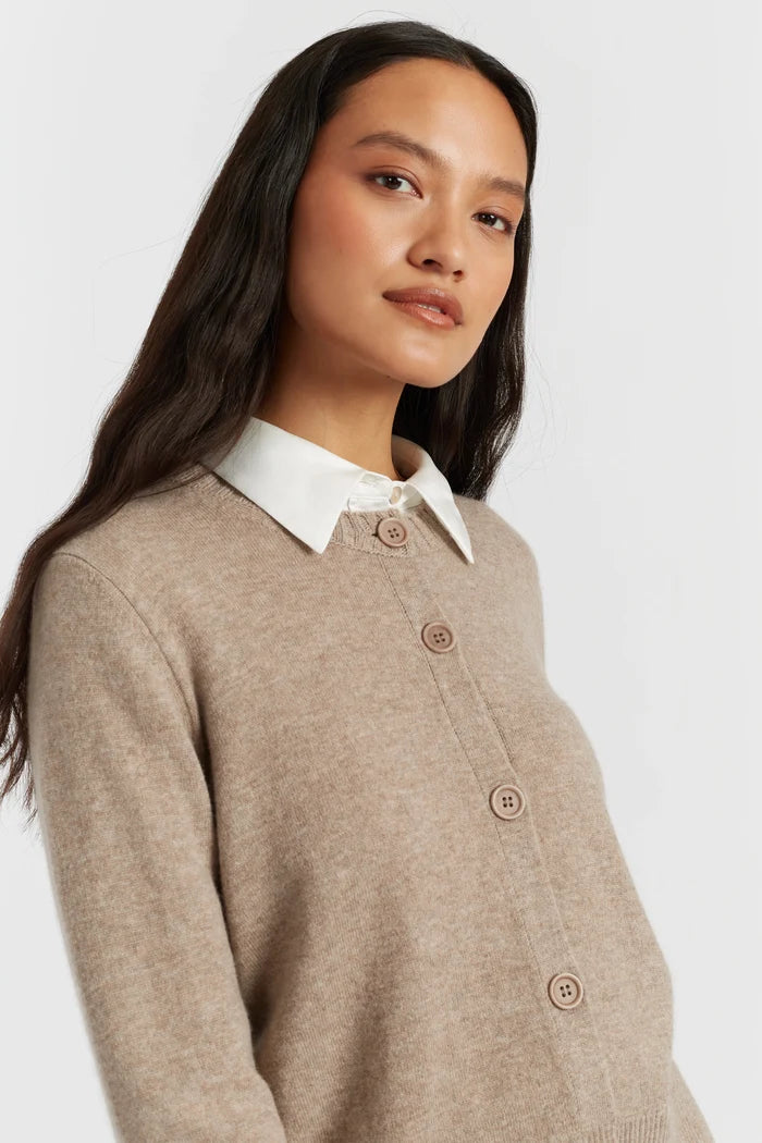 Woman wearing a beige cardigan over a white shirt on a plain background